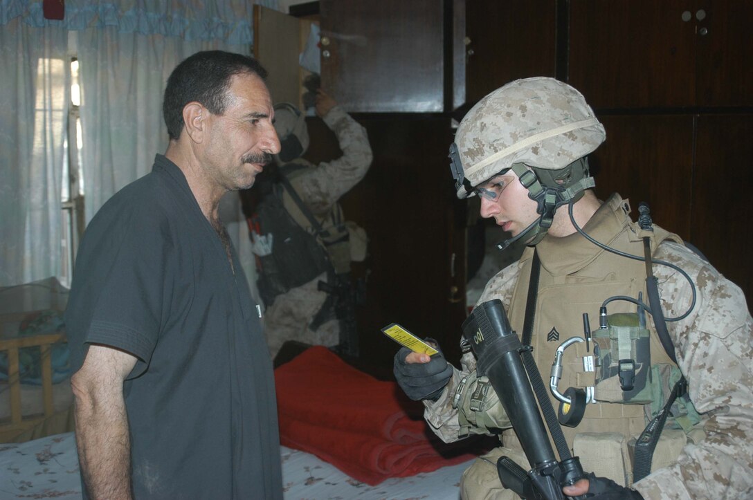 AR RAMADI, Iraq (May 8, 2005) -Sergeant Jade C. Hill, the squad leader of 3rd Squad, 2nd Platoon, Company A, 1st Battalion, 5th Marine Regiment, checks an Iraqi man's identification while one of his fellow Marines looks through his closet during a search mission in the city here. The 21-year-old from Westminster, Md., and other warriors with the infantry battalion's Company's A, C and W conducted "Operation Weston," which was a three-hour cordon and search mission of a neighborhood. The purpose of the mission was to eradicate the area of insurgents and inform the people living there of the consequences for harboring terrorists. The Marines hit three improvised explosive devises and found one 155 mm shell. One Marine received minor shrapnel wounds, and no insurgents were captured. Photo by Cpl. Tom Sloan