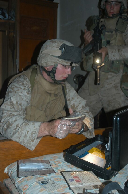 AR RAMADI, Iraq (May 7, 2005) - Twenty-one-year-old Pfc. Andrew R. Schwartz from Billings, Mont., and a grenadier with 3rd Squad, 2nd Platoon, Company A, 1st Battalion, 5th Marine Regiment, searches the contents of a brief case during an operation here. Twenty-year-old Cpl. Adam C. Daigle from Cromwell, Conn., and a rifleman and team leader with 3rd Squad, 2nd Platoon, Company A, helps his comrade see by shining the flashlight mounted on his weapon. The infantry battalion's Company's A, C and W conducted "Operation Weston," which was a three-hour cordon and search mission of a neighborhood. The purpose of the mission was to eradicate the area of insurgents and inform the people living there of the consequences for harboring terrorists. The Marines hit three improvised explosive devises and found one 155 mm shell. One Marine received minor shrapnel wounds, and no insurgents were captured. Photo by Cpl. Tom Sloan