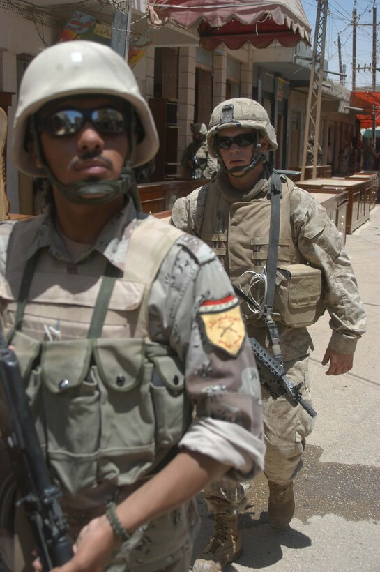 AR RAMADI, Iraq (June 7, 2005) - A member of the Iraqi Security Forces patrols down a street in the marketplace here during a mission. Lance Cpl. Ethan P. Claypool ,a squad automatic weapon gunner with 3rd Squad, 1st Platoon, Company A, 1st Battalion, 5th Marine Regiment, follows behind. The 20-year-old from Marshall, Ill., and his fellow Company A Marines searched several buildings on a mile-long stretch of road that bisects the city's marketplace during "Operation Weatherford III." Two squads of ISF assisted the Marines during the three-hour mission, which was aimed at finding sniper positions, weapons caches, improvised explosive device making material and suspicious individuals. Photo by: Cpl. Tom Sloan