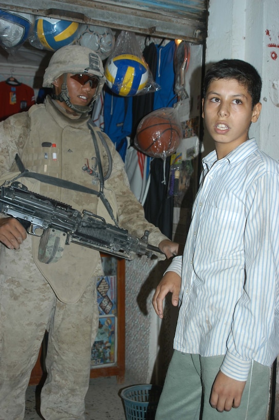 AR RAMADI, Iraq (June 7, 2005) - Lance Cpl. Lou N. Coloma, squad automatic weapon gunner with 3rd Squad, 1st Platoon, Company A, 1st Battalion, 5th Marine Regiment, talks to an Iraqi boy during a mission in the marketplace here. The 23-year-old Filipino from Chicago and his fellow Company A Marines searched several buildings on a mile-long stretch of road that bisects the city's marketplace during "Operation Weatherford III." Two squads of Iraqi Security Forces assisted the Marines during the three-hour mission, which was aimed at finding sniper positions, weapons caches, improvised explosive device making material and suspicious individuals. Photo by: Cpl. Tom Sloan
