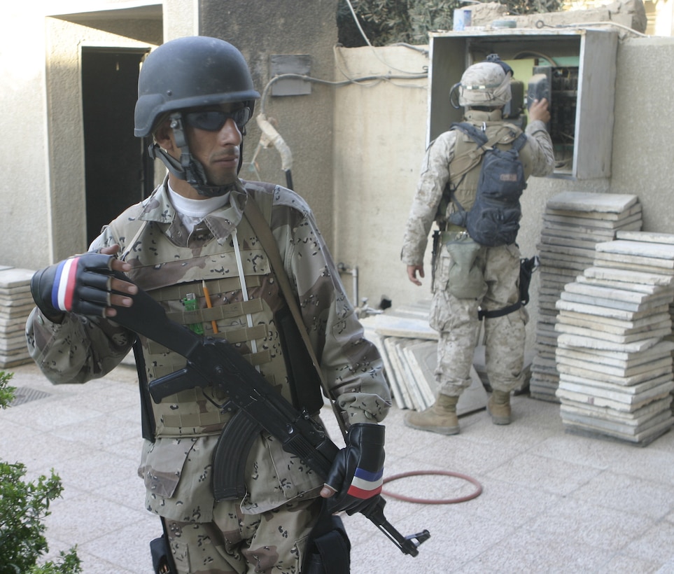 FALLUJAH, Iraq - An Iraqi soldier provides security outside a home here July 7 while Marines search the perimeter for arms and insurgent activity.  Iraqi Security Forces assisted Company B, 1st Battalion, 6th Marine Regiment personnel conduct Operation Hard Knock, during which the troops wired off entire neighborhoods and searched through each house for concealed weapons and explosives.