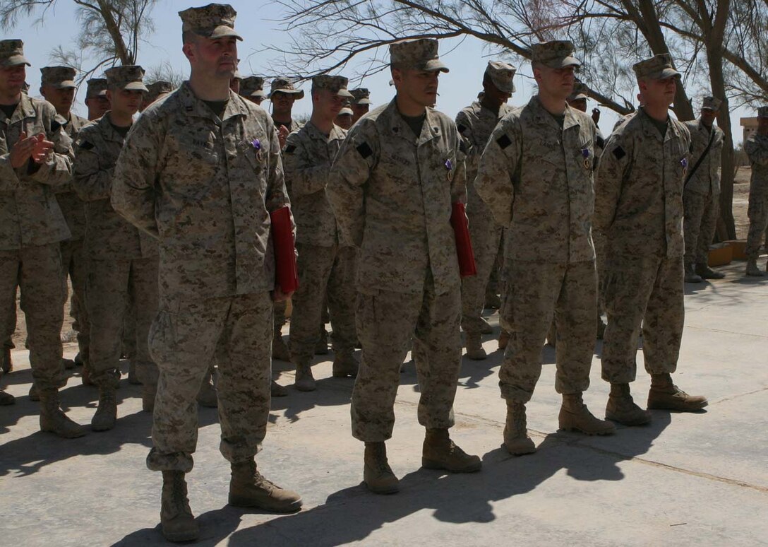 CAMP FALLUJAH, IRAQ - Lined up in front of the formation, Capt. William G. Rayne, Sgt. Jorge H. Herrera, Lance Cpl. Joshua C. Landis and Lance Cpl. Curt L. Smith stand at ease while their fellow Marines applaud them for their valiant efforts during the day of the election when the building they were in was shot by a rocket propelled grenade.  Official U.S. Marine Corps photo by Lance Cpl. Athanasios L. Genos