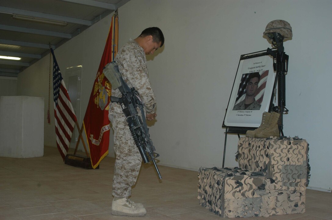 CAMP RAMADI Ar Ramadi, Iraq (June 7, 2005) - Corporal Eduardo Munoz, a grenadier and team leader with 1st Squad, 4th Platoon, Company B, 1st Battalion, 5th Marine Regiment, stands in front of Cpl. Jeff B. Starr's monument, bows his head and pays tribute to the late Company B warrior during a memorial ceremony here. Starr was killed May 30, Memorial Day, by small arms fire while conducting operations against enemy forces in this city. Munoz, a 24-year-old from Mission, Texas, and scores of Marines from the infantry battalion attended the ceremony to honor their comrade who paid the ultimate price while fighting terror on the urban battlefield. Photo by: Cpl. Tom Sloan