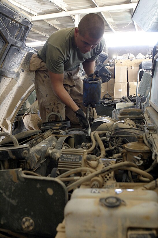 CAMP BAHARIA, Iraq - Lance Cpl. Joshua Sanchez, a maintenance management specialist with 1st Battalion, 6th Marine Regiment's motor transport section, pours power steering fluid into a High Mobility Multi-Wheeled Vehicle here June 8.  The battalion's Motor 'T' Marines service several military trucks' engines, transmissions and electric systems, along with freighting fuel and water to locations throughout the camp and Fallujah.