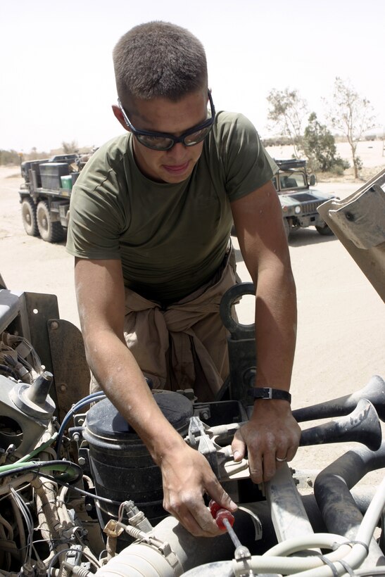 CAMP BAHARIA, Iraq - Lance Cpl. Kyle Hutcheon, a mechanic with 1st Battalion, 6th Marine Regiment's motor transport section, inspects components underneath a seven-ton truck's hood here June 8.  The battalion's Motor 'T' Marines service several military trucks' engines, transmissions and electric systems, along with freighting fuel and water to locations throughout the camp and Fallujah.