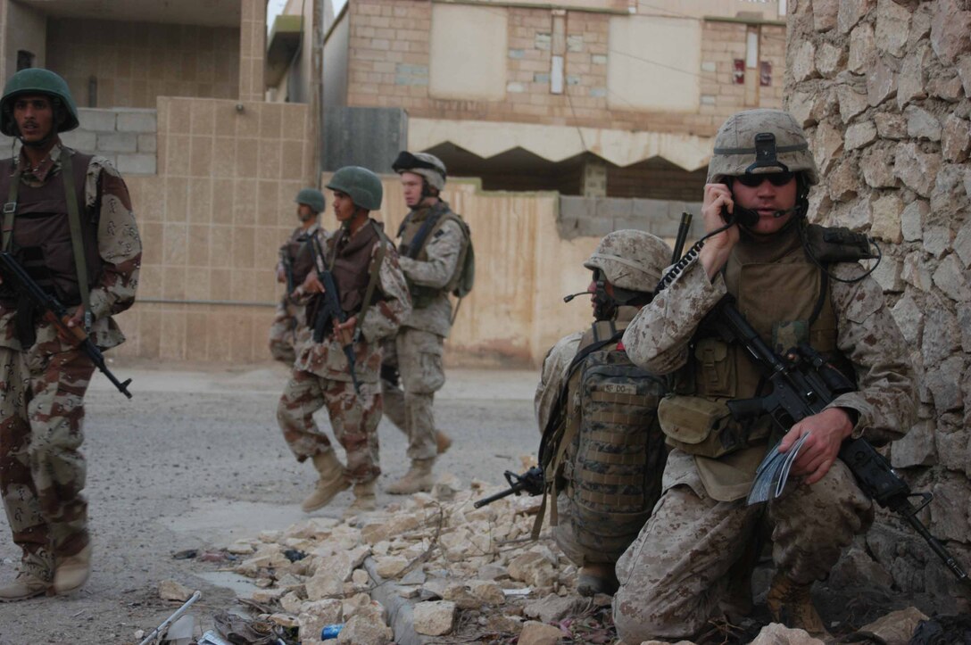 AR RAMADI, Iraq (Aug. 8, 2005) -Second Lieutenant Michael L. Burke, platoon commander, Combined Action Platoon(CAP), Company B, 1st Battalion, 5th Marine Regiment, takes a knee and communicates with his Marines during a foot patrol through a portion of the city here with Iraqi Security Forces. Burke's radio operator, Cpl. Peter H. Do, 21, of Beaverton, Ore., kneels down behind him and provides security. Combined Action Platoon Marines support Operation Iraqi Freedom by training new members of the ISF and employing them on Ramadi's urban battlefield to help secure the city from terrorism. The Marines are letting the ISF carry more of the operational workload because their tactics are improving. Iraqi Security Forces are even leading their own foot patrols. Photo by: Cpl. Tom Sloan