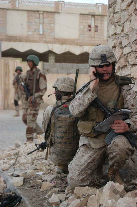 AR RAMADI, Iraq (Aug. 8, 2005) -Second Lieutenant Michael L. Burke, platoon commander, Combined Action Platoon(CAP), Company B, 1st Battalion, 5th Marine Regiment, takes a knee and communicates with his Marines during a foot patrol through a portion of the city here with Iraqi Security Forces. Burke's radio operator, Cpl. Peter H. Do, 21, of Beaverton, Ore., kneels down behind him and provides security. Combined Action Platoon Marines support Operation Iraqi Freedom by training new members of the ISF and employing them on Ramadi's urban battlefield to help secure the city from terrorism. The Marines are letting the ISF carry more of the operational workload because their tactics are improving. Iraqi Security Forces are even leading their own foot patrols. Photo by: Cpl. Tom Sloan