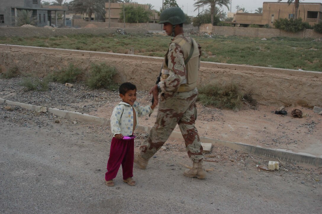 AR RAMADI, Iraq (Aug. 8, 2005) - An Iraqi child greets a member of the Iraqi Security Forces during a patrol through the city here Aug. 8. Many of the Al Anbar capital's locals respond well to having ISF patrol through their neighborhoods conducting security and stabilization operations. Marines with the Combined Action Platoon(CAP), Company B, 1st Battalion, 5th Marine Regiment, support Operation Iraqi Freedom by training new members of the ISF and employing them on Ramadi's urban battlefield to help secure the city from terrorism. The Marines are letting the ISF carry more of the operational workload because their tactics are improving. Iraqi Security Forces are even leading their own foot patrols. Photo by: Cpl. Tom Sloan