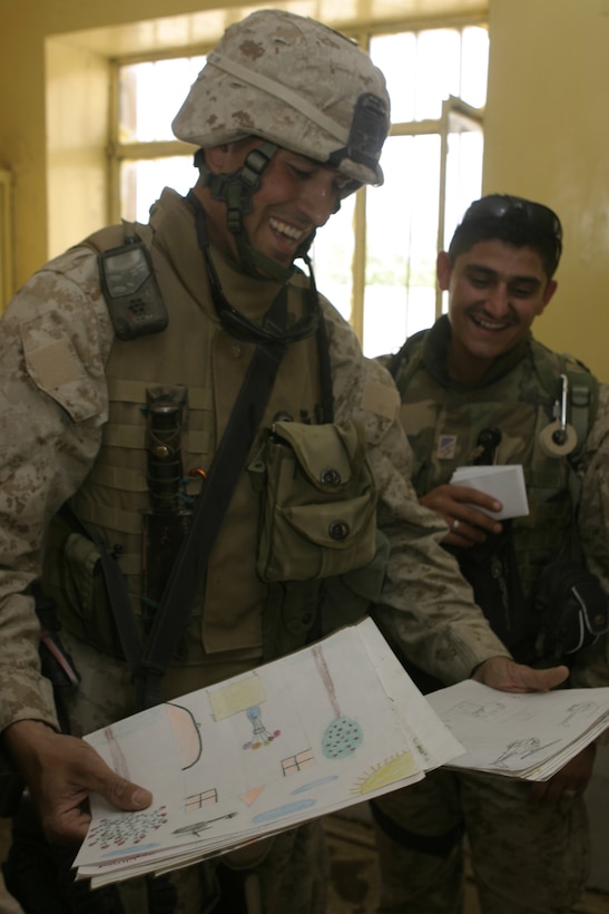 SAQLAWIYAH, Iraq - Maj. Chris E. Phelps, team leader for 1st Battalion, 6th Marine Regiment's civil affairs group, left, and his interpreter, Mustafa, look at drawings children at a local school they helped improve gave them May 9.  Phelps' CAG Marines traveled with Oliver North throughout the city, showing him the progress the Iraqi soldiers and Marines here have made restoring the city's infrastructure.