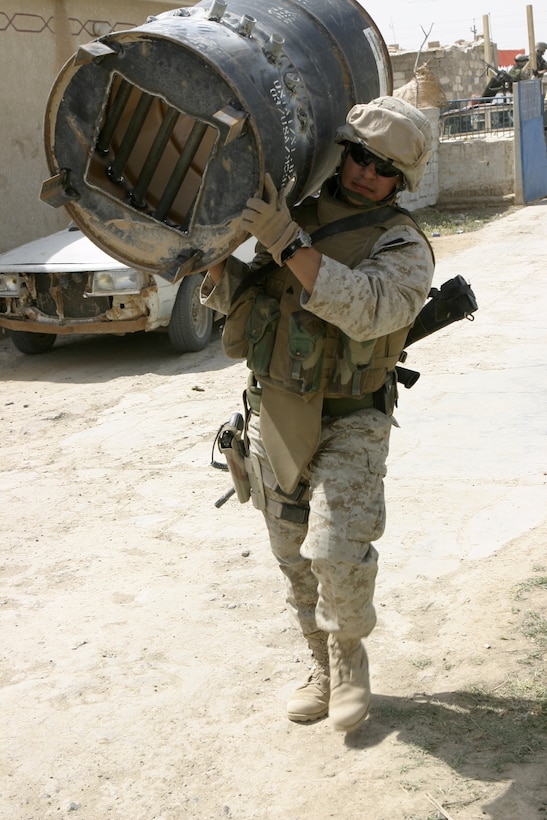 SAQLAWIYAH, Iraq - Cpl. Ramon Ramos, Headquarters and Service Company, 1st Battalion, 6th Marine Regiment's police sergeant, carries in a makeshift incinerator into the medical clinic here May 9.  Marines like Ramos accompanied Oliver North throughout the city, showing him the progress the Iraqi soldiers and Marines here have made restoring the city's infrastructure.