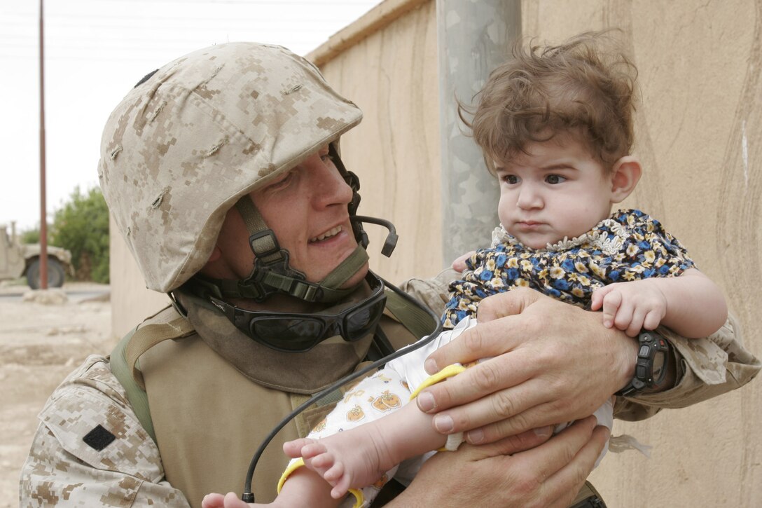 South Dam Village, Al Anbar, Iraq.--  Maj. Todd C. Waldemar holds an Iraqi infant during a recent civil affairs mission in South Dam Village.  The Marines spent several hours talking to residents about insurgent activity, particularly mortar attacks.  Kids received soccer balls, school supplies, and candy from the Marines.      (Photo by LCpl. Marc Fencil. )