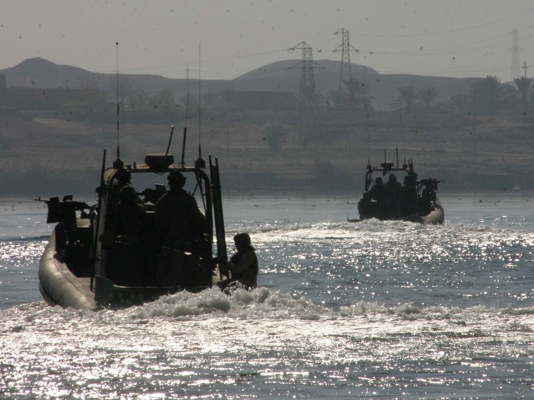 HADITHA DAM, Iraq ? Staff Sgt. Matthew J. Lockwood, a Galveston, Texas native and section leader for the Dam Security Unit, looks through the binoculars as the boat?s coxswain points to a suspicious area on shore during a patrol Dec. 9. The unit, currently attached to 3rd Battalion, 1st Marine Regiment, keeps the waters around the dam safe for the thousands of Iraqi people who depend on the dam for their power.