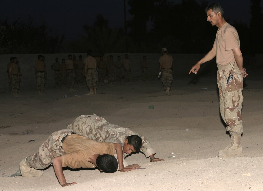 FALLUJAH, Iraq - An Iraqi troop leader "motivates" his troops by supervising them as they conduct push-ups as part of their early morning physical training routine.  PT is incorporated into the "Lion Training" package, which teaches Iraqi soldiers the fundamentals of marksmanship, basic first aid, and military customs and courtesies.