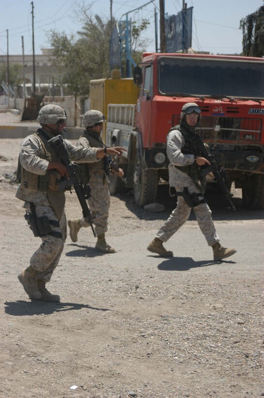 AR RAMADI, IRAQ (May 10, 2005) - With his weapon in the alert position, Sgt. Hector Martinez Jr., noncommissioned officer with Team 1, Detachment 3, 5th Civil Affairs Group, shows his team leader, Maj. Benjamin B. Busch,(right) the site where they need to inspect minor property damage done to two businesses in the city here. Their translator(middle) accompanies them. The civil affairs Marines conducted a detailed battle site assessment of two automotive shops that elements of 1st Battalion, 5th Marine Regiment, damaged during a recent cordon and search mission. Marines with 5th CAG will ensure the owners are properly compensated for the damages incurred to their establishments. Photo by Cpl. Tom Sloan