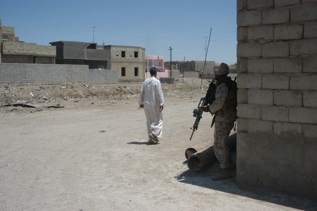 AR RAMADI, IRAQ (May 10, 2005) - An Iraqi man walks past Sgt. Hector Martinez Jr., noncommissioned officer with Team 1, Detachment 3, 5th Civil Affairs Group, while he provides security for his fellow civil affairs Marines so they can inspect an area in the city here. The 28-year-old from Fontana, Calif., and his fellow civil affairs Marines conducted a detailed battle site assessment of two automotive shops that elements of 1st Battalion, 5th Marine Regiment, damaged during a recent cordon and search mission. Marines with 5th CAG will ensure the owners are properly compensated for the damages incurred to their establishments. They also assessed other areas in the city they believe need improving. Photo by Cpl. Tom Sloan