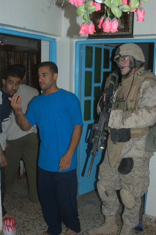 AR RAMADI Iraq (July 10, 2005) - Corporal Mike J. White, a mortar man with 4th Platoon, Company W, 1st Battalion, 5th Marine Regiment, posts security by Iraqi men while other Marines search their house during a mission in the city here early July 10. The 25-year-old from Eden Prairie, Minn., and fellow Marines with 3rd and 4th Platoon conducted a raid between 1 a.m. and 3 a.m., during which time they captured an insurgent responsible for launching small arms and improvised explosive device(IED) attacks on coalition forces. Photo by: Cpl. Tom Sloan