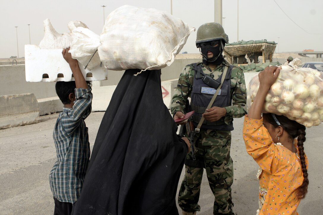 FALLUJAH, Iraq - An Iraqi policeman speaks with local citizens and checks their credentials aboard Fallujah's Entry Control Point-One before admitting them into the city Aug. 10.  Marines with 1st Battalion, 6th Marine Regiment oversee Iraqi policemen with the Public Order Brigade as they search the thousands of automobiles and local citizens entering the city every day for weapons and contraband.