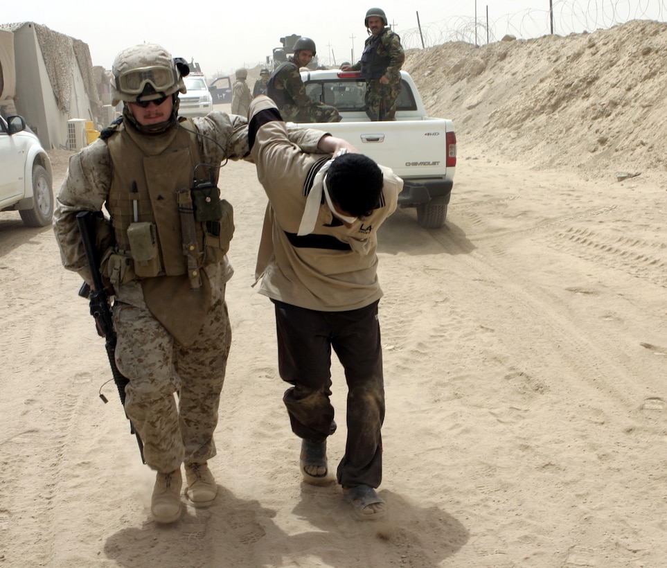 FALLUJAH, Iraq - Cpl. Jason T. Johnson, a sergeant of the guard at 1st Battalion, 6th Marine Regiment's Entry Control Point-One "Alpha," escorts an insurgent that policemen with the Public Order Brigade apprehended here Aug. 10.  Iraqi Security Forces and U.S. Marines apprehended a total of four suspected terrorists for weapons possession, emplacing roadside bombs, and possible involvement in a nearby firefight.