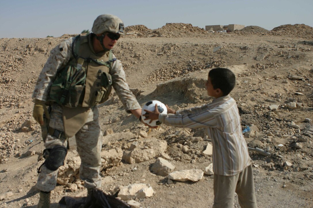 Iraq - Lance Cpl. Jose H. Garcia Jr., a Mebane, N.C. native and team member of the 6th Civil Affairs Group, Detachment Three, Team Five, hands a soccer ball to a child here Oct. 10. Giving soccer balls and other toys to children they meet helps improve relations with the people in the city.