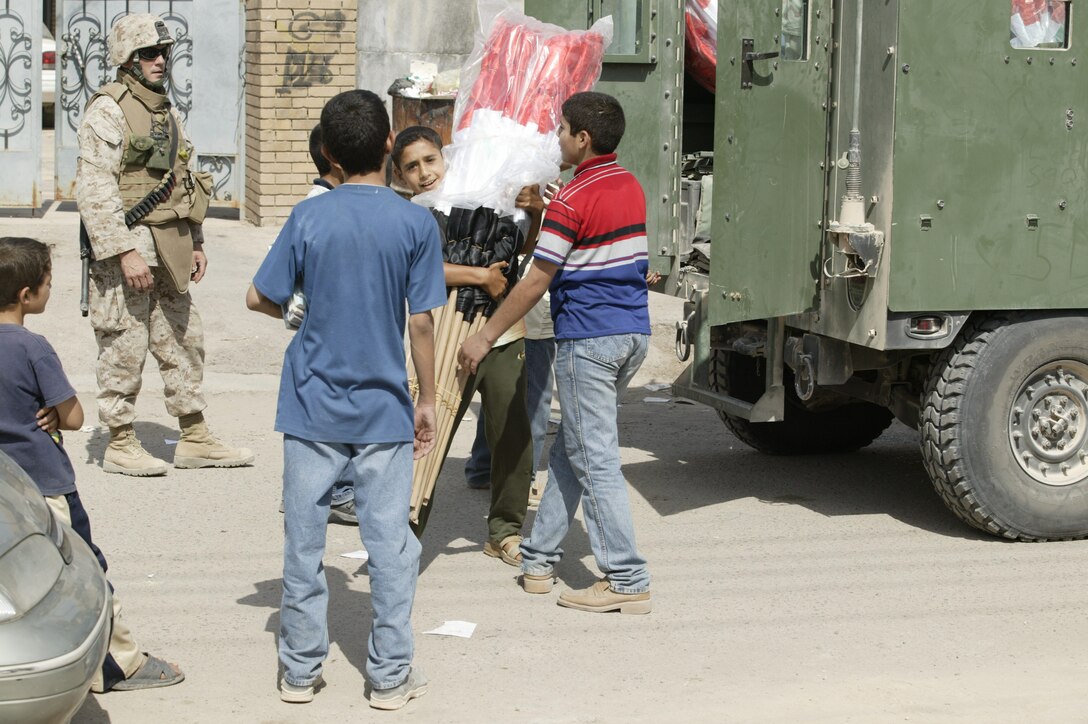 Gunnery Sgt. Kevin S. Tuite, team chief, Team 4, Det. 4., 6th Civil Affairs Group, 2nd Marine Division, and a native of Sterling, Pa., watches as the children of Iraq help carry bundles of their country?s flag into the Ministry of Education?s office in Fallujah.