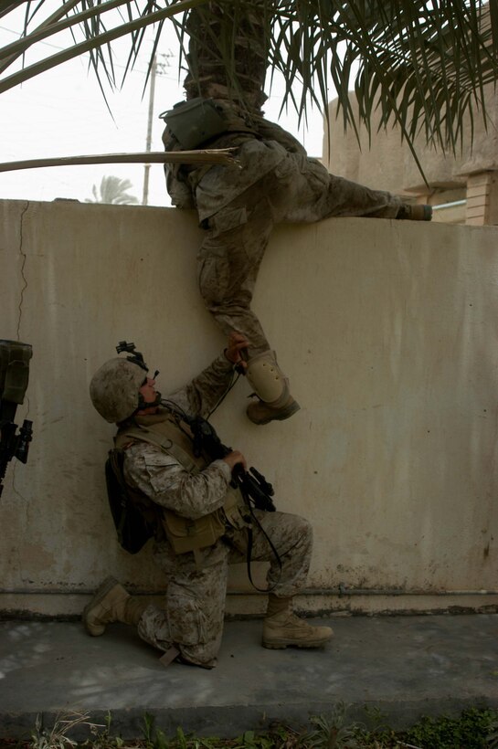 AR RAMADI Iraq (June 11, 2005) - Staff Sgt. Joshua W. Raposa, the platoon sergeant for 5th Mobile Assault Platoon, Company W, 1st Battalion, 5th Marine Regiment, helps one of his Marines climb over a wall during a mission in the city here. The 31-year-old from Albany, N.Y., and his fellow warriors conducted a presence patrol in the southern part of the city in an effort to uncover insurgent activity and deter them from operating. The platoon was engaged by an enemy sniper and hit an improvised explosive device during the operation. No one was hurt and no vehicles were damaged. Photo by: Cpl. Tom Sloan.