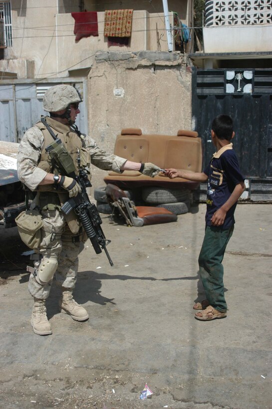 AR RAMADI, Iraq (April 11, 2005) - Lance Cpl. Jordan P. Marshall, a grenadier with 2nd Squad, 1st Platoon, Company A, 1st Battalion, 5th Marine Regiment, gives an Iraqi boy a Tootsie Roll during a patrol through the city here with his fellow squad members. The 22-year-old Ventura, Calif., native and his fellow leathernecks with 2nd Squad, 1st Platoon, Company A, 1st Battalion, 5th Marines, have become familiar with their area of operations where they conduct security and stability operations almost daily. They've learned to recognize landmarks to help determine what particular street they're patrolling. First Battalion, 5th Marines are two months into their seven-month deployment here in support of Operation Iraqi Freedom. Photo by Cpl. Tom Sloan