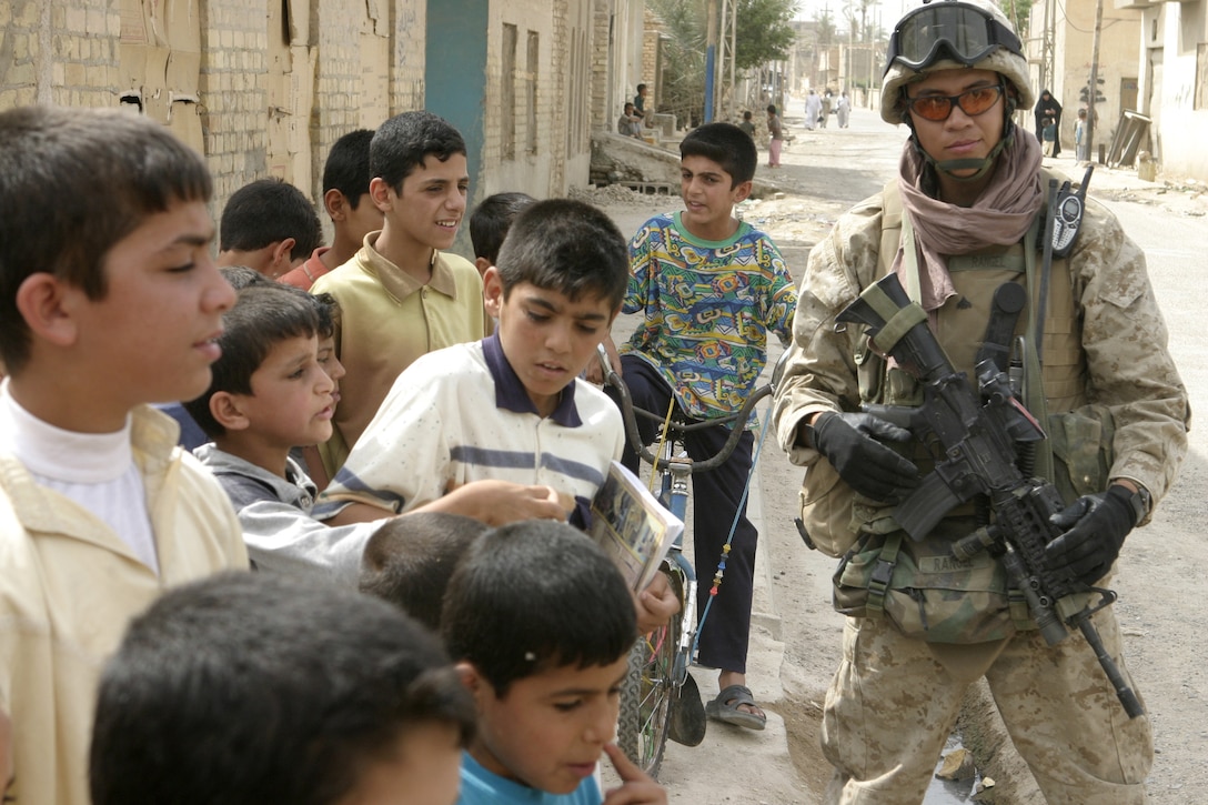 FALLUJAH, Iraq -.Cpl. Alexandro C. Rangel, an infantryman with Company C, 1st Battalion, 6th Marine Regiment, provides security outside a school here May 12 while he interacts with the children.  Rangel's unit and Iraqi Security Forces are currently conducting 'Operation Blackboard,' a joint civil-military mission during which Iraqi soldiers re-supply Fallujah's schools and continue winning the citizens' trust.