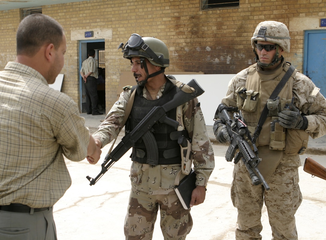 FALLUJAH, Iraq - 1st. Lt. Anthony Mercado, Company C, 1st Battalion, 6th Marine Regiment's executive officer, observes as an Iraqi soldier shakes hands and speaks with teachers outside a school here May 12.  1st Battalion, 6th Marine Regiment is currently working with Iraqi Security Forces to conduct 'Operation Blackboard,' a joint civil-military mission during which Iraqi soldiers re-supply Fallujah's schools and continue winning the citizens' trust.