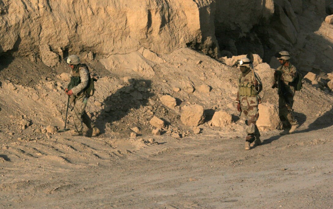 050921-M-2607O-003 CAMP FALLUJAH, Iraq -- A Marine from Combat Engineer Platoon attached to 2d Battalion, 2d Marine Regiment, along with Iraqi Soldier of the 1-4-1 search an area for weapons caches along a road in the area of operation.  The Iraqi Soldiers received classes the day before to prepare them for the cache sweep.