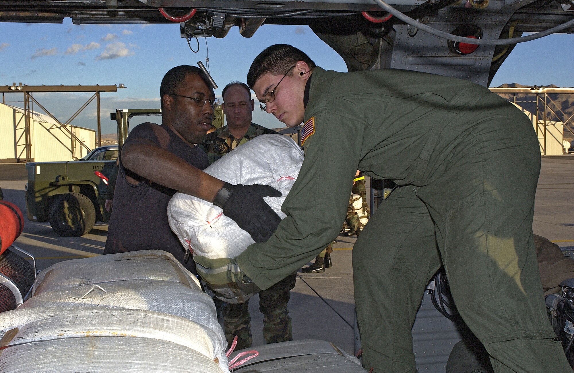 NELLIS AIR FORCE BASE, Nev. -- Staff Sgt. Leo Cruz (right) and Senior Airman Reginald Hobbs load bundles of empty sandbags onto an HH-60G Pave Hawk helicopter here Jan. 11.  Four helicopters from here and a C-130 Hercules from the Nevada Air National Guard delivered the sandbags and evacuated 118 students and 19 staff members from a youth center in Caliente, Nev., after flooding cut off ground access to the facility.  Sergeant Cruz is an aerial gunner assigned to the 66th Rescue Squadron here; Airman Hobbs is an avionics specialist assigned to the 763rd Maintenance Squadron.  (U.S. Air Force photo by Airman 1st Class Daniel DeCook)