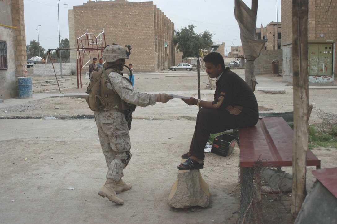 AR RAMADI, Iraq (April 9, 2005) - Staff Sgt. Ramon E. Gonzales, platoon sergeant, 2nd Platoon, Company C, 1st Battalion, 5th Marines, hands an Iraqi man a positive and anti-insurgent propaganda pamphlet during a patrol through a neighborhood here known as the "Ghetto." Patrols here often include interaction with Iraqi children. Photo by Cpl. Tom Sloan