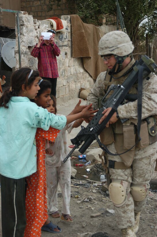 AR RAMADI, Iraq (April 9, 2005) -Corporal Jeremy B. Herndon, a 25-year-old rifleman with 2nd Squad, 2nd Platoon, Company C, 1st Battalion, 5th Marine Regiment, reaches in his pockets for candy to give to smiling Iraqi children during a patrol through their neighborhood here known as the "Ghetto." The Christmas Valley native and other Marines with 2nd Squad, 2nd Platoon, Company C, 1st Battalion, 5th Marines, patrolled the neighborhood and handed out candy to the children and positive and anti-insurgent propaganda pamphlets to Iraqi men. Photo by Cpl. Tom Sloan