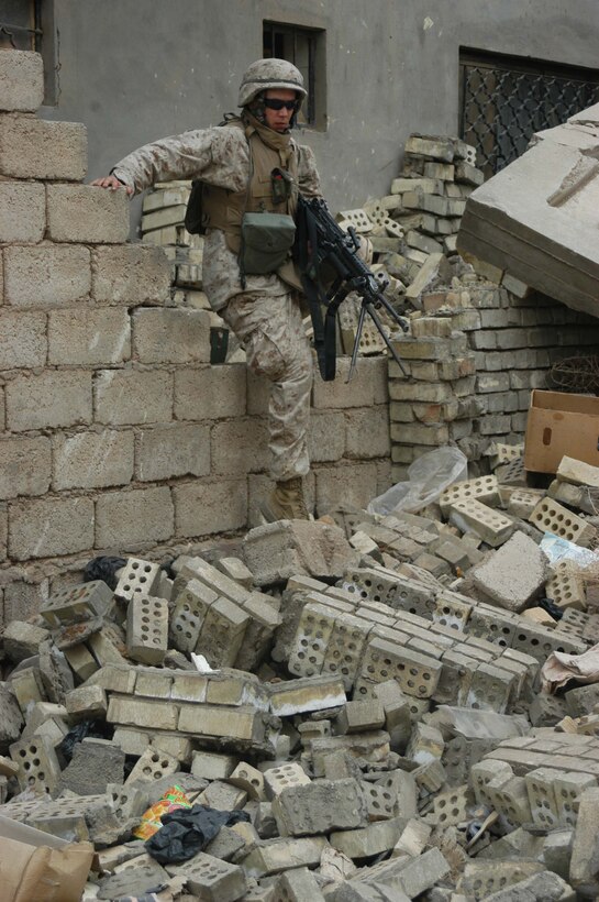 AR RAMADI, Iraq (April 9, 2005) - Lance Cpl. Donald A. Owens, a 23-year-old squad automatic weapon gunner with 2nd Squad, 2nd Platoon, Company C, 1st Battalion, 5th Marine Regiment, climbs over a brick wall as he exits a building he and his Marines used as an over watch during a patrol through a neighborhood here known as the "Ghetto." The Cleburne, Texas, native and other Marines with 2nd Squad, 2nd Platoon, Company C, 1st Battalion, 5th Marines, patrolled the neighborhood and handed out candy to the children and positive and anti-insurgent propaganda pamphlets to Iraqi men. Photo by Cpl. Tom Sloan