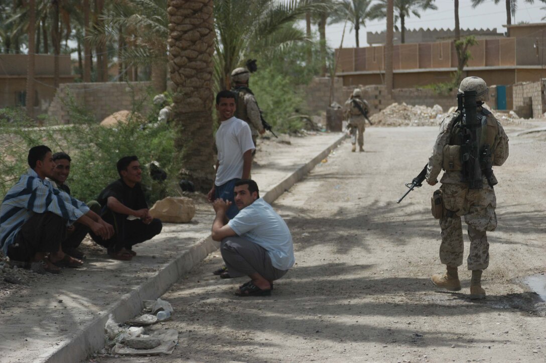 AR RAMADI, Iraq (May 13, 2005) - A group of Iraqi men sit under the shade of a palm tree in the city here while Marines with 2nd Platoon, Company B, 1st Battalion, 5th Marine Regiment, pass by during a patrol. Warriors with 2nd Platoon conducted a three-hour presence patrol through a portion of their company's area of operations notorious for insurgent activity. The Marines encountered sporadic machine gun fire from insurgents during their mission, which was geared toward disrupting enemy activity. The Marines accomplished their mission and returned to their firm base, Camp Ramadi, safely. Photo By: Cpl. Tom Sloan