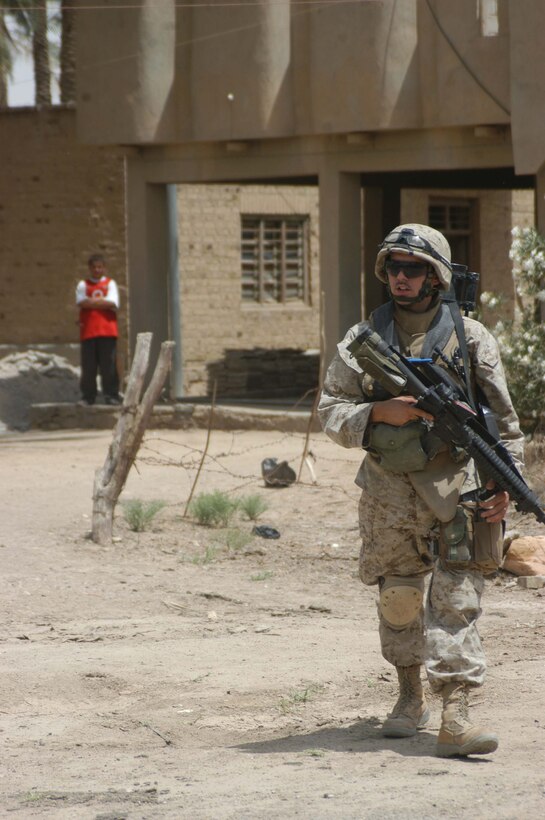 AR RAMADI, Iraq (May 13, 2005) - Standing from afar, an Iraqi boy watches Lance Cpl. Justin R. Corry, an assault man with 2nd Squad, 2nd Platoon, Company B, 1st Battalion, 5th Marine Regiment, passes through his neighborhood here during a patrol. The 19-year-old Jackson, Mich., native and his fellow 2nd Platoon warriors conducted a three-hour presence patrol through a portion of their company's area of operations notorious for insurgent activity. The Marines encountered sporadic machine gun fire from insurgents during their mission, which was geared toward disrupting enemy activity. The Marines accomplished their mission and returned to their firm base, Camp Ramadi, safely. Photo By: Cpl. Tom Sloan