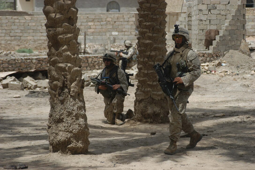 AR RAMADI, Iraq (May 13, 2005) -Private First Class Bryan J. Nagel, a squad automatic machine gunner with 2nd Squad, 2nd Platoon, Company B, 1st Battalion, 5th Marine Regiment, walks past his comrade, Lance Cpl. Justin R. Corry, an assault man with 2nd Squad, 2nd Platoon, who took a knee under the shade of a palm tree in the city here during a patrol. Nagel, 20, of Jamestown, N.D., and his fellow 2nd Platoon warriors conducted a three-hour presence patrol through a portion of their company's area of operations notorious for insurgent activity. The Marines encountered sporadic machine gun fire from insurgents during their mission, which was geared toward disrupting enemy activity. The Marines accomplished their mission and returned to their firm base, Camp Ramadi, safely. Photo By: Cpl. Tom Sloan