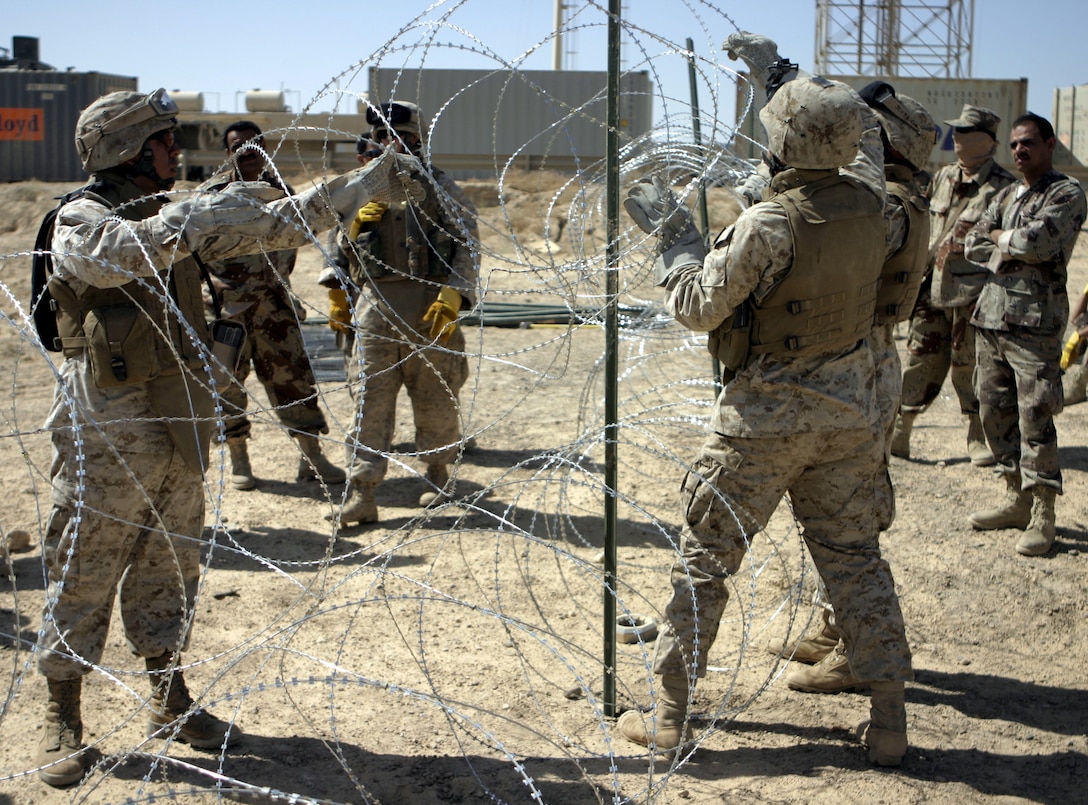 FALLUJAH, Iraq - Marine combat engineers and Iraqi soldiers construct a double-strand concertina wire fence here June 13.  Marines with 2nd Platoon, Company A, 2nd Combat Engineer Battalion instructed the soldiers on how to string various types of wires, board up windows and fortify defensive positions.