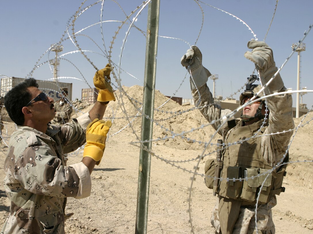 FALLUJAH, Iraq - Lance Cpl. Jason Murray, a team leader with 2nd Squad, 2nd Platoon, Company A, 2nd Combat Engineer Battalion, helps an Iraqi soldier put up a strand of concertina wire here June 13.  Marine engineers instructed the soldiers on how to string various types of wires, board up windows and fortify defensive positions.