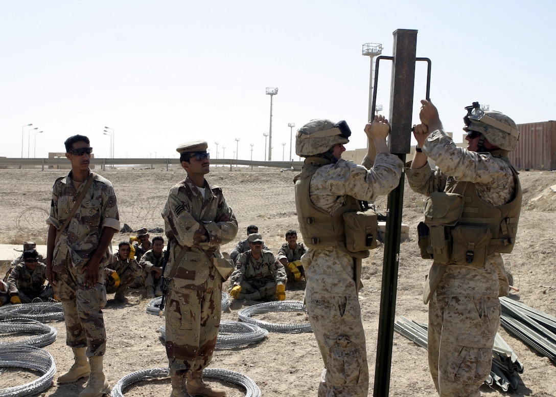 FALLUJAH, Iraq - Marine combat engineers with 2nd Platoon, Company A, 2nd Combat Engineer Battalion show Iraqi soldiers how to hammer an engineer stake into the ground here June 13 to prepare for the construction of a wire fence.  The Marines instructed the soldiers on how to string various types of wires, board up windows and fortify defensive positions.