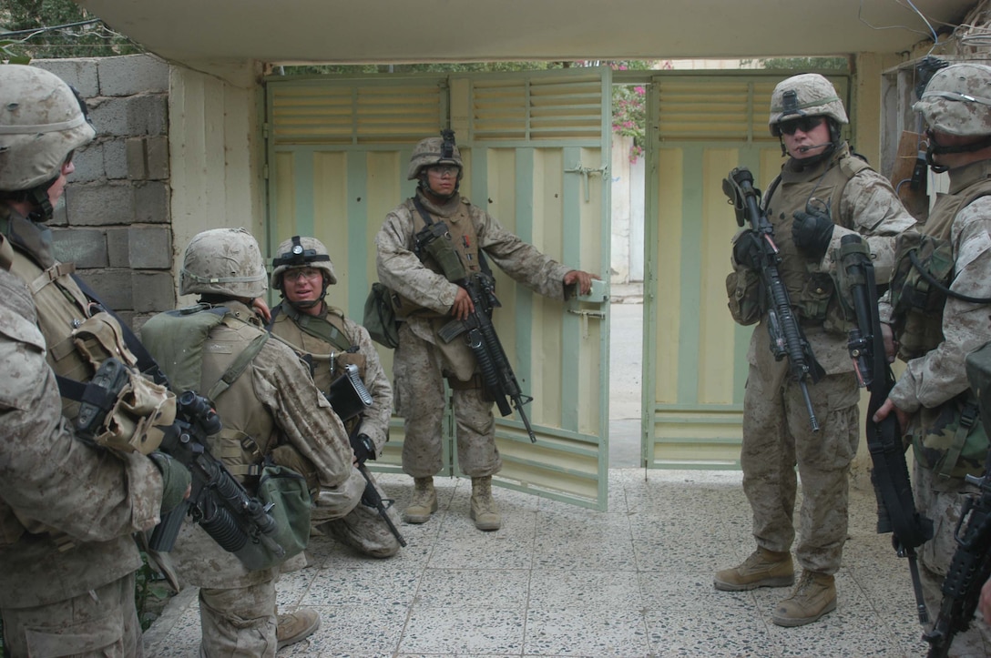 CAMP HURRICANE POINT Ar Ramadi, Iraq (July 13, 2005) - Lance Cpl. Miguel A. Bautista(center), a rifleman with Company A, 1st Battalion, 5th Marine Regiment, stands behind the door of a residency in the city here and prepares to enter the street during a mission July 12. The 19-year-old from Dallas and his high school friend, Lance Cpl. Christopher J. Gonzalez, who's also 19-years-old, are both in Ar Ramadi, Iraq supporting Operation Iraqi Freedom with Camp Pendleton, Calif., based 1st Battalion, 5th Marines. Gonzalez is a food service specialist with Headquarters and Service Company. The two friends chose the road less traveled after graduating from North Dallas High School in 2004 and enlisted in the Marine Corps. Photo by: Cpl. Tom Sloan