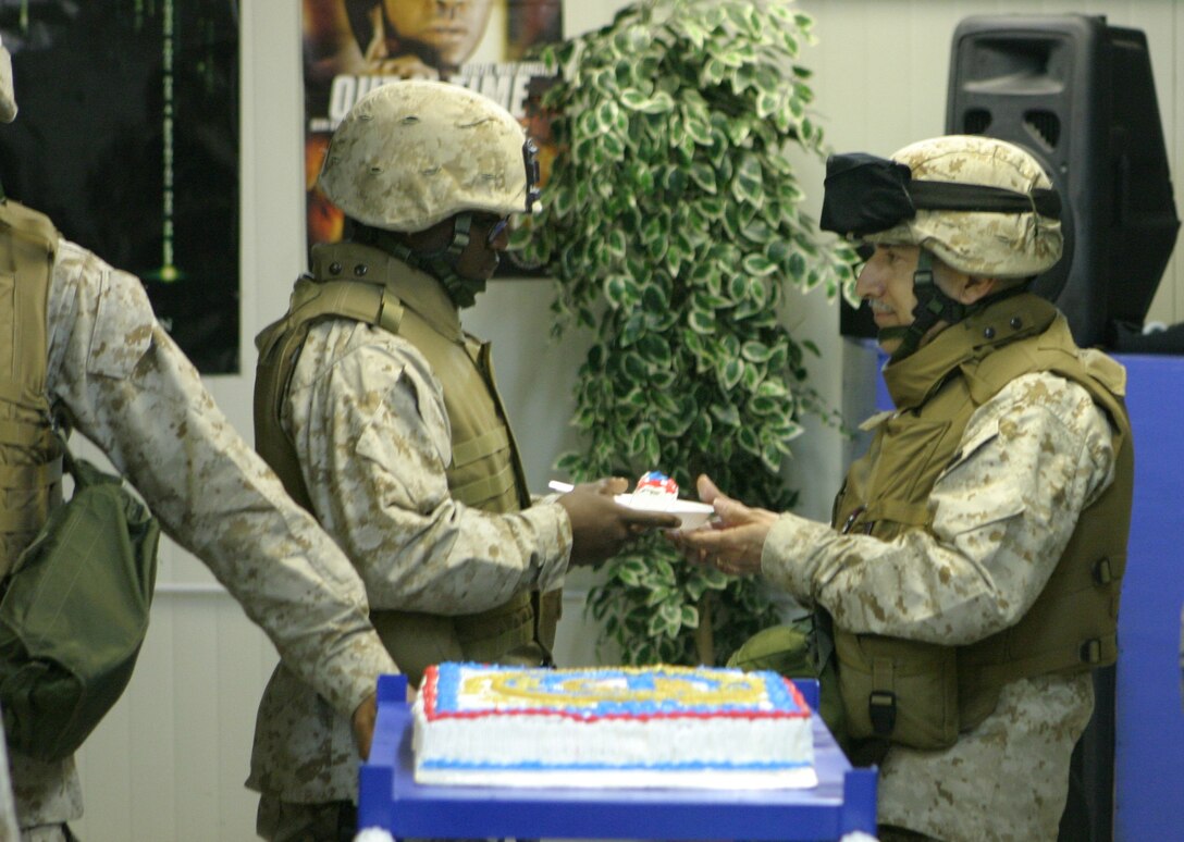 CAMP BLUE DIAMOND, AR RAMADI, Iraq - Commander Robert Puder, left, present a piece of the traditional birthday cake to Darius Evans, right, during a ceremony for the 230th birthday of the Navy. The passing of the cake from oldest to youngest sailor present signifies the passing of heritage to those who follow and will lead the Navy into the future. Service members with the 2nd Marine Division celebrated the Navy's birthday with a traditional cake cutting ceremony.
