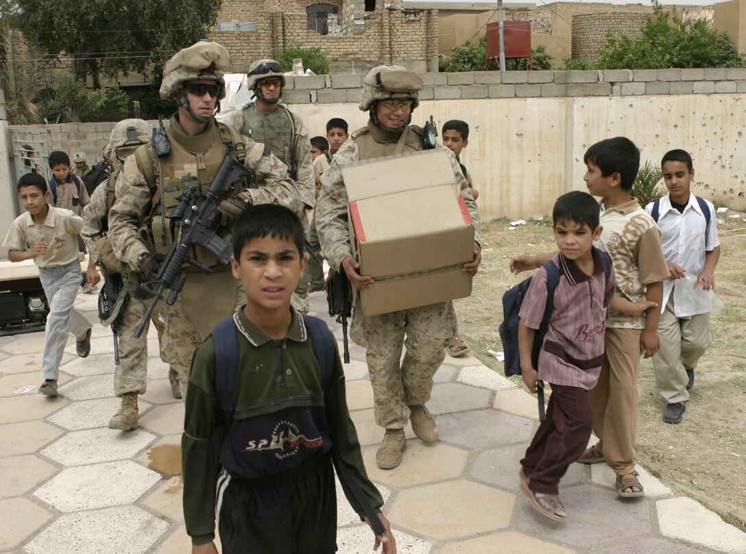 FALLUJAH, Iraq - 1st Lt. Thomas Waller, executive officer for Company B, 1st Battalion, 6th Marine Regiment, left, and Sgt. Royes Gernandt, a machine gun section leader with Company B, right, carry boxes of writing supplies and walk toward a school here May 2.  Iraqi Security Forces and Marines here visited local schools to distribute blackboards, school desks, and writing supplies as part of the ongoing joint civil-military mission, "Operation Blackboard."