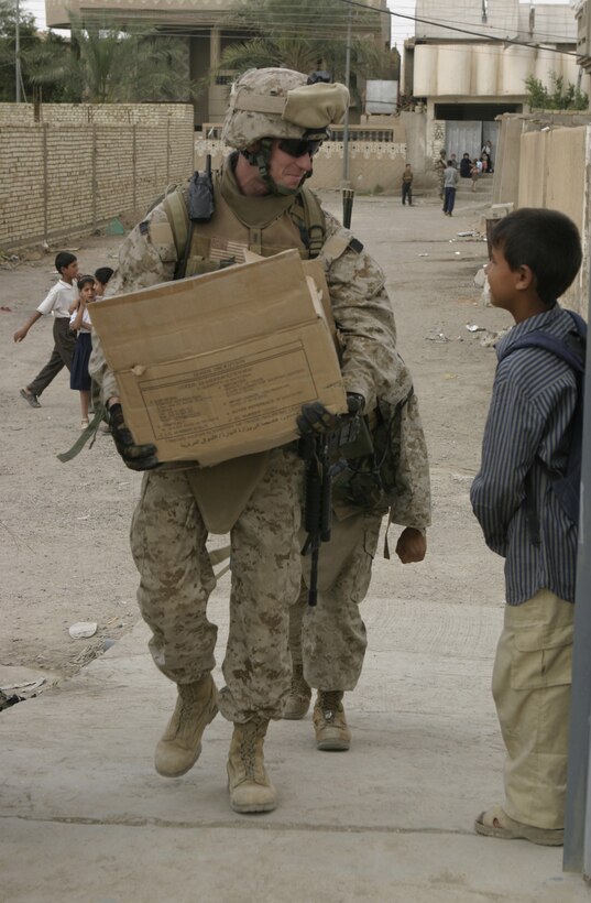 FALLUJAH, Iraq - 1st Lt. Thomas Waller, executive officer for Company B, 1st Battalion, 6th Marine Regiment, smiles at a local child as he carries a box of writing supplies and walks toward a school here May 2.  Iraqi Security Forces and Marines here visited local schools to distribute blackboards, school desks, and writing supplies as part of the ongoing joint civil-military mission, "Operation Blackboard."