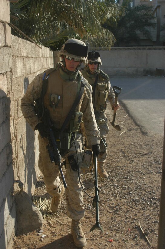 AR RAMADI, Iraq (May 7, 2005) - Armed with his weapon and metal detector, 20-year-old Lance Cpl. Robert O. Page from Nashville, Tenn., and a combat engineer with 1st Combat Engineer Battalion, walks quickly alongside a street here as he heads to his next position. Corporal Jason T. Ekeland, 22, of Newton, Kansas, and a fellow combat engineer with 1st CEB, follows closely behind. The two blast masters assisted Marines with 1st Battalion, 5th Marine Regiment, in conducting "Operation Weston." The infantry battalion's Company's A, C and W conducted the operation, which was a three-hour cordon and search mission of a neighborhood. The purpose of the mission was to eradicate the area of insurgents and inform the people living there of the consequences for harboring terrorists. The Marines hit three improvised explosive devises and found one 155 mm shell. One Marine received minor shrapnel wounds, and no insurgents were captured. Photo by Cpl. Tom Sloan