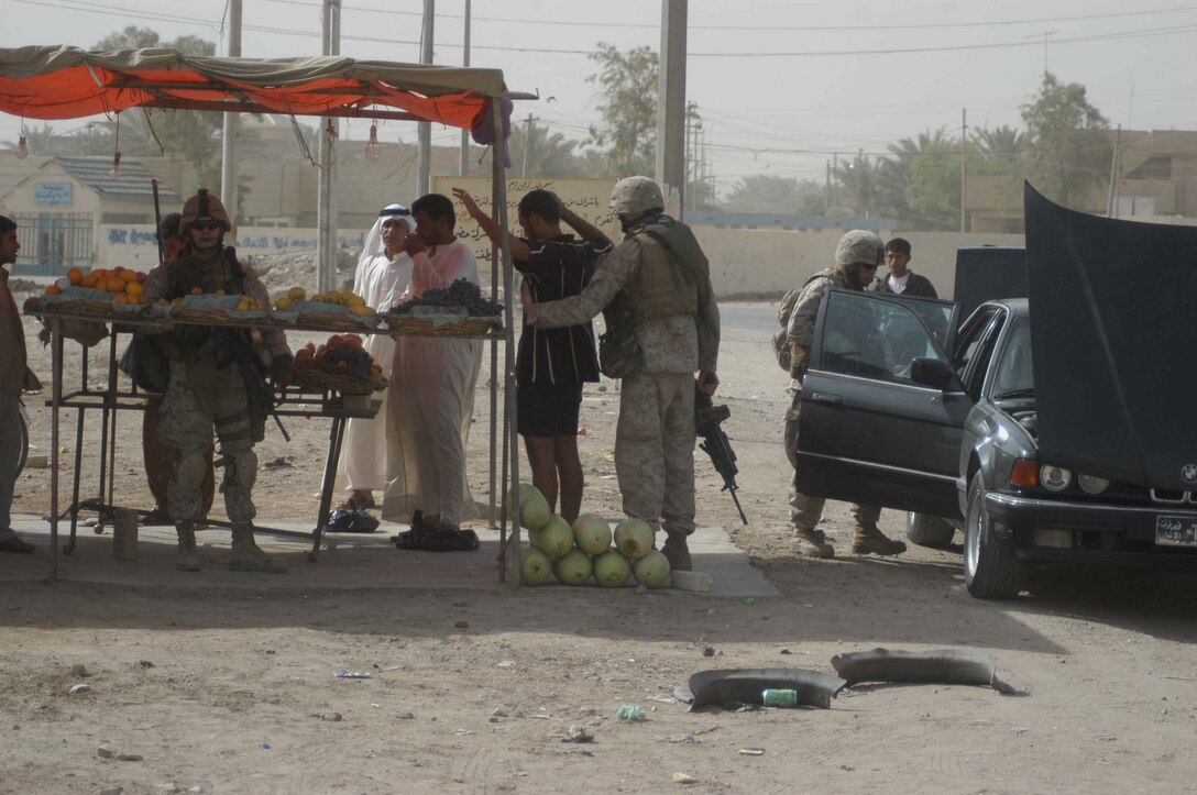 AR RAMADI Iraq (July 16, 2005) - Marines with Company A, 1st Battalion, 5th Marine Regiment, search Iraqi men at a corner store and parked cars in the Al Anbar capital city July 14 during Operation Fire. Marines with the Camp Pendleton, Calif., based infantry battalion stopped traffic in various parts of the city and conducted vehicle and personnel searches during the three-hour operation, which netted the capture of seven insurgents. Photo by: Cpl. Tom Sloan