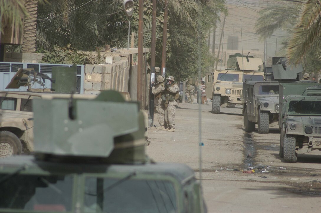 AR RAMADI Iraq (July 16, 2005) - A Marine with Company A, 1st Battalion, 5th Marine Regiment, provides security while one of his comrades posts a coalition forces flier on a light pole in the Al Anbar capital city July 14 during Operation Fire. Marines with the Camp Pendleton, Calif., based infantry battalion stopped traffic in various parts of the city and conducted vehicle and personnel searches during the three-hour operation, which netted the capture of seven insurgents. Photo by: Cpl. Tom Sloan