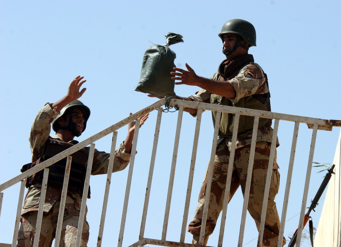 AR RAMADI, Iraq (Oct. 14, 2005) - Two soldiers from the Iraqi Security Force toss sand bags to help reinforce the roof of the election sites in preparation of the national constitutional referendum vote held Oct. 15. Photo by Cpl. Shane Suzuki