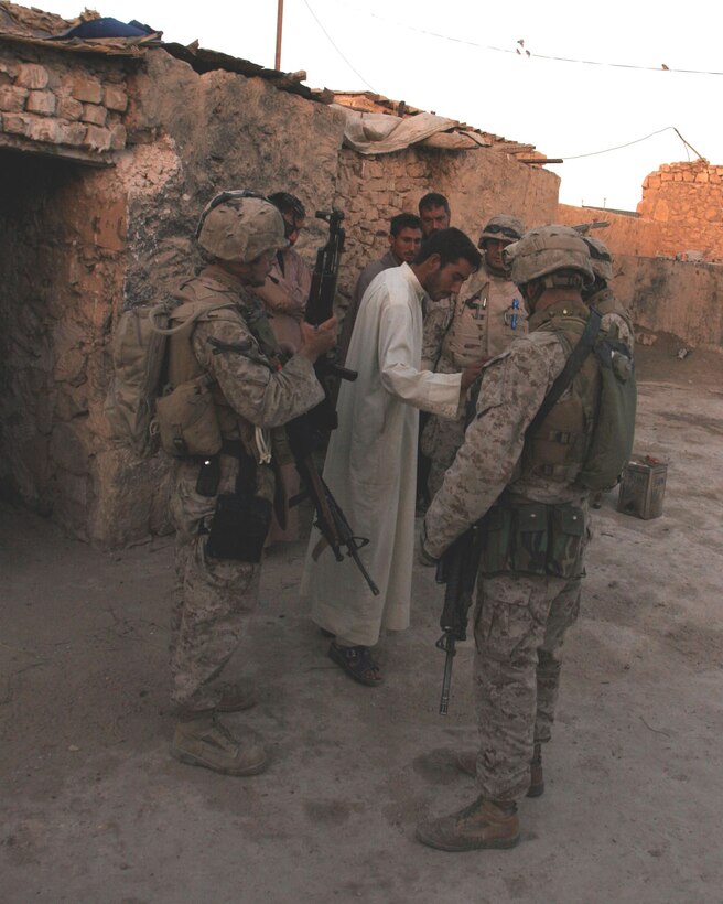 Cpl. Chris W. Adair (left) holds a rifle found by his squad while they talk to three military-aged males (MAMs) during a "knock and talk" patrol outside of Fallujah.