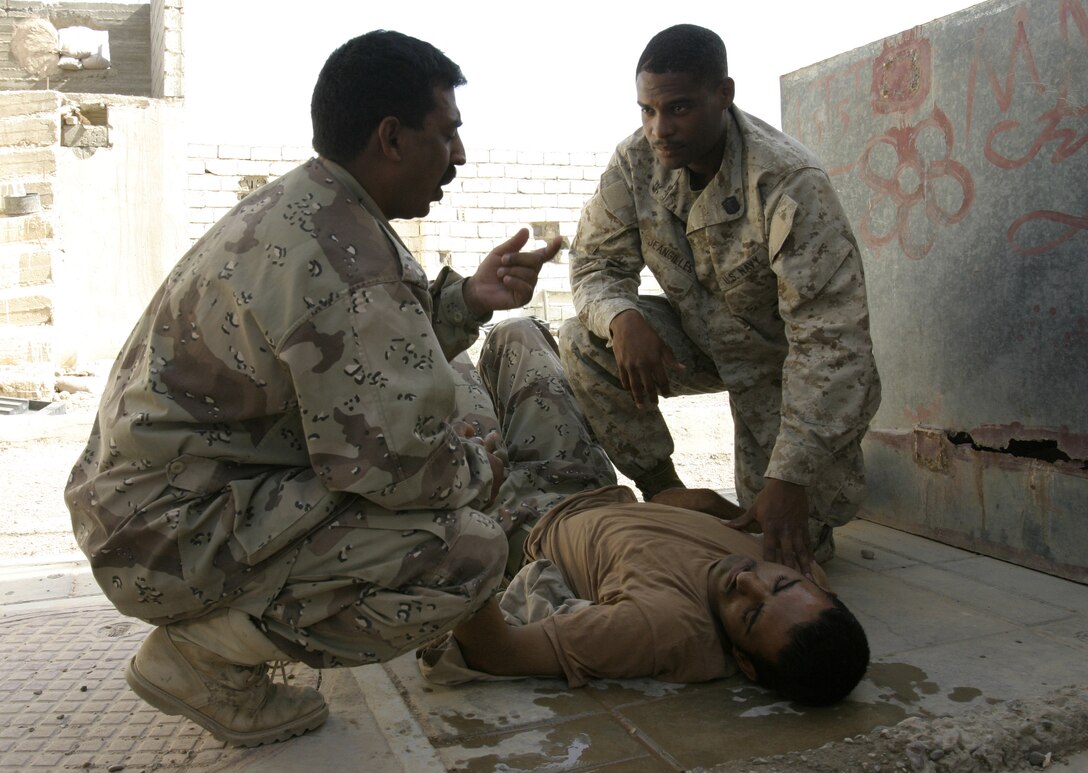 FALLUJAH, Iraq - Navy Petty Officer 2nd Class Phillip Jean-Gilles, a corpsman with 1st Battalion, 6th Marine Regiment, assesses an Iraqi soldier's condition alongside another soldier at a training compound here May 11.  The 26-year-old Miami native and 1st Battalion, 6th Marine Regiment infantrymen tended to a dehydrated Iraqi soldier while teaching a five-day Iraqi combat leaders course.