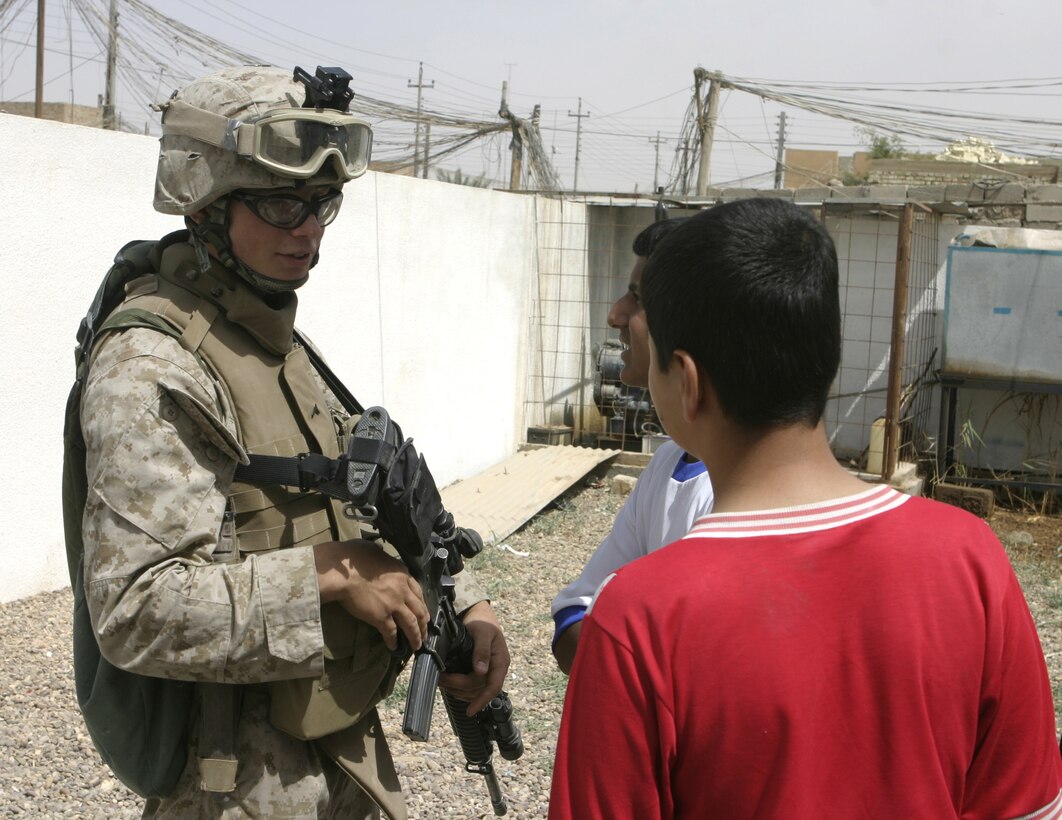 FALLUJAH, Iraq - Pfc. Jason F. Roland, rifleman with 3rd Squad, 2nd Platoon, Company B, 1st Battalion, 6th Marine Regiment, speaks with local children as he provides security outside a medical clinic here May 15.  The Seaford, N.Y. native's unit worked alongside Iraqi Security Forces to speak with local doctors and clinic administrators to find out what supplies they needed, and how military personnel can help improve Iraq's medical system.